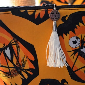 May include: A yellow and black zippered pouch with a white tassel. The pouch features a repeating pattern of Jack Skellington and Sally from the Nightmare Before Christmas.