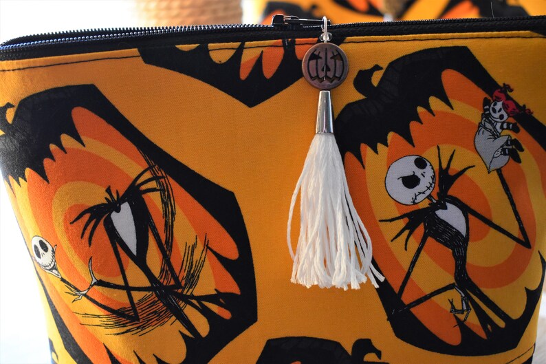May include: A yellow and black zippered pouch with a white tassel. The pouch features a repeating pattern of Jack Skellington and Sally from the Nightmare Before Christmas.