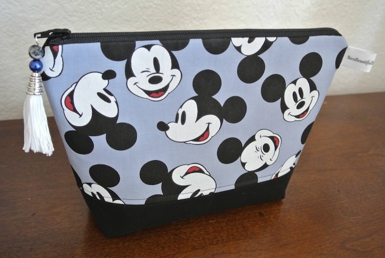May include: A blue and black zippered pouch with a Mickey Mouse print. The pouch has a black zipper and a black tassel.