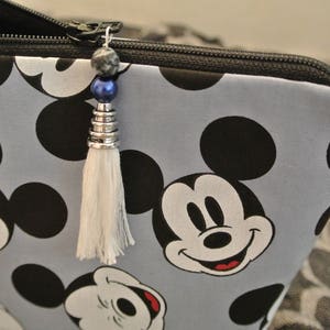 May include: A grey zippered pouch with a Mickey Mouse print. The pouch has a white tassel with a blue and silver bead charm.