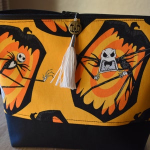 May include: A yellow zippered pouch with a black and white print of Jack Skellington from The Nightmare Before Christmas. The pouch has a black zipper and a white tassel with a pumpkin charm.