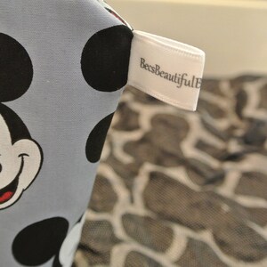 May include: A light blue fabric with a Mickey Mouse design and black polka dots. The fabric has a white tag with the text "BeesBeautiful" on it.