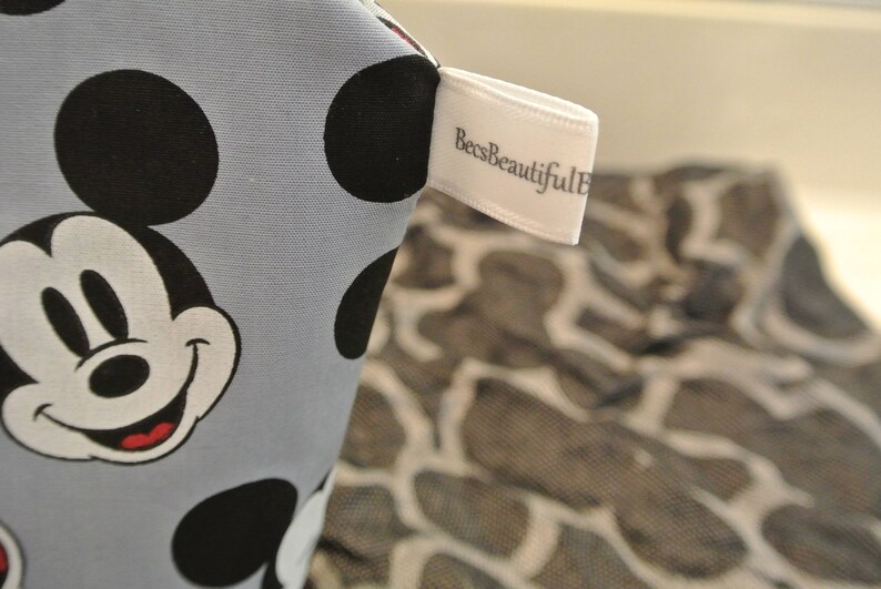 May include: A light blue fabric with a Mickey Mouse design and black polka dots. The fabric has a white tag with the text "BeesBeautiful" on it.
