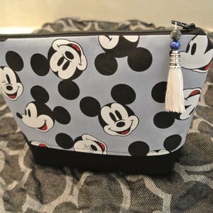 May include: A blue and black zippered pouch with a Mickey Mouse print. The pouch has a black tassel with blue and silver beads.