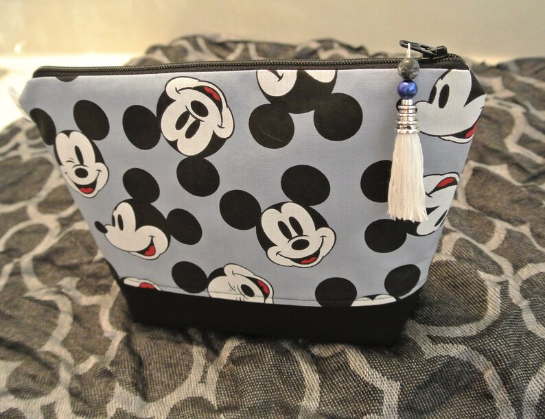 May include: A blue and black zippered pouch with a Mickey Mouse print. The pouch has a black tassel with blue and silver beads.