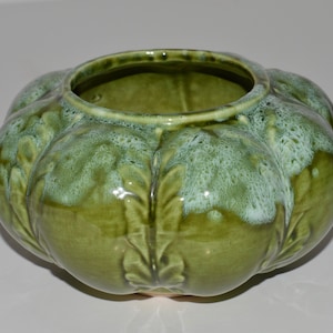 May include: A green ceramic planter with a textured, leafy design. The planter has a rounded, bulbous shape and a wide opening.