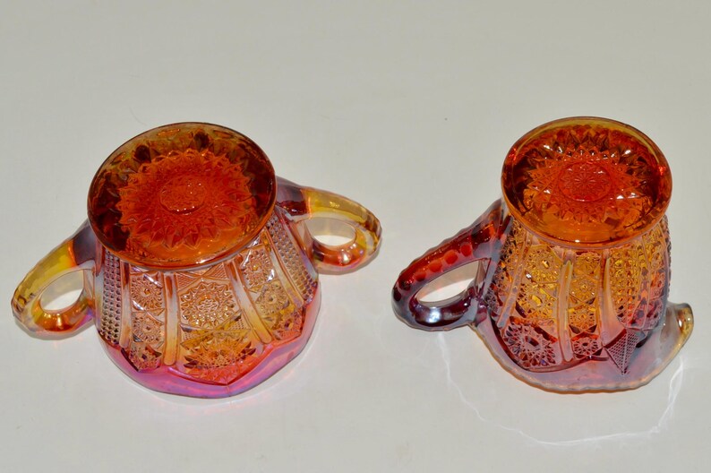 May include: A set of two vintage glass sugar bowls with a cranberry and amber iridescent finish. The bowls have a scalloped edge and a floral design.