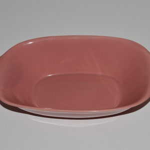 May include: A pink ceramic serving bowl with two handles. The bowl is oval shaped and has a slightly raised center.