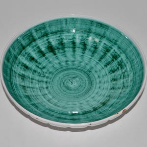 May include: A round ceramic bowl with a teal and white design. The interior of the bowl features a teal spiral pattern, while the rim is white with a scalloped edge. The bowl is likely used for serving food.