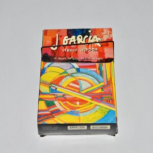 May include: A colorful box of "Street Wisdom" art cards by J. Garcia. The box features a vibrant abstract design with a mix of colors, including yellow, red, blue, and green. The title and artist's name are printed on the top of the box.