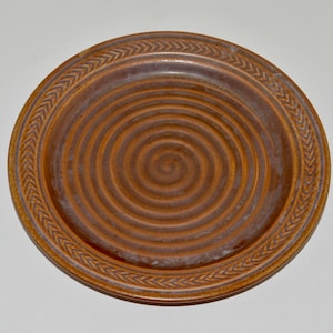 May include: A brown ceramic plate with a spiral design and a braided rim.