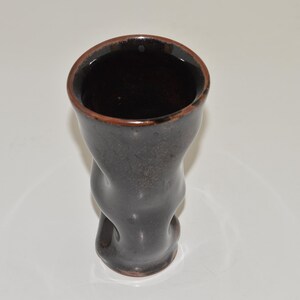 May include: A dark brown ceramic vase with a unique, wavy design. The vase has a wide opening and a narrow base.