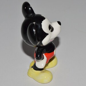 May include: A vintage Mickey Mouse figurine. The figure is primarily black and white, with red shorts and yellow shoes. The figurine is standing and has a classic cartoon appearance.