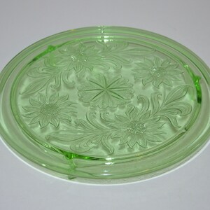 May include: A green glass cake plate with a floral design. The plate has three feet and is perfect for serving desserts.