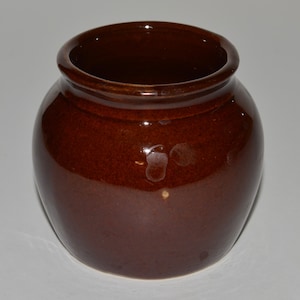 May include: A small, brown ceramic pot with a rounded body and a slightly flared rim. The pot has a glossy finish and is perfect for holding small plants or other decorative items.