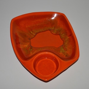 May include: A ceramic serving dish with a divided section and a smaller round dip bowl. The dish is orange with a mottled glaze and a gold-like shimmer.