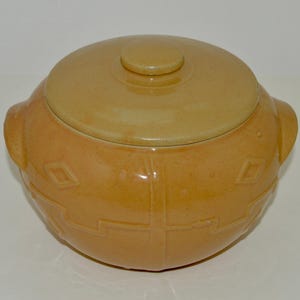 May include: A yellow ceramic cookie jar with a lid. The jar has a geometric design and a knob on the lid.