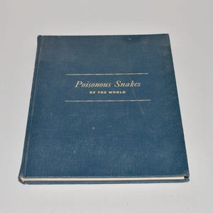 May include: A hardcover book titled "Poisonous Snakes of the World" in white text on a blue cover. The book has a rectangular shape and is lying flat. The cover has two horizontal lines above and below the title.