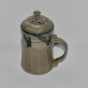 May include: A ceramic salt shaker with a lid and a handle. The shaker is decorated with a green and brown glaze.