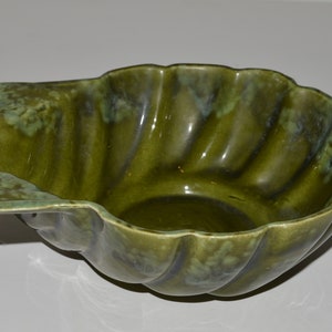 May include: A green ceramic bowl with a scalloped edge and a unique, organic shape. The bowl has a mottled glaze with shades of green and blue.