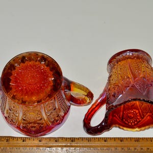 May include: A set of two vintage glass creamer and sugar bowls in a cranberry color with a detailed floral pattern.