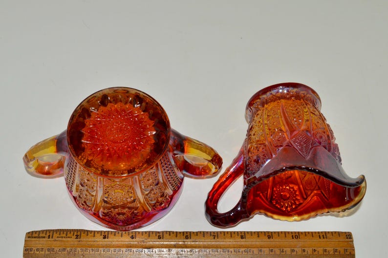 May include: A set of two vintage glass creamer and sugar bowls in a cranberry color with a detailed floral pattern.
