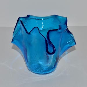 May include: A blue glass vase with a ruffled, wavy design. The vase is made of clear glass with a blue tint.