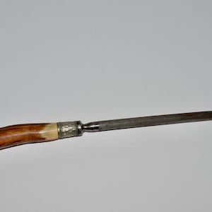 May include: A knife sharpener with a wooden handle and a metal blade. The handle is a light brown color with a cream-colored section near the metal. The blade is a dark gray color.