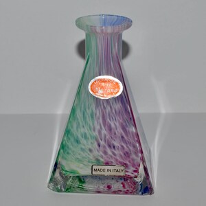 May include: A colorful glass vase with a triangular shape. The vase is made in Italy and features a blend of green, purple, and blue hues. The vase has a flared top and a label that says "Murano".
