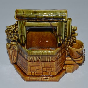 May include: A ceramic wishing well planter with a green roof, brown brick base, and a metal chain with a bucket. The well has a square opening and the words "Wishing Well" are inscribed on the front.