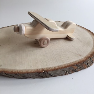 May include: A wooden toy airplane with a propeller and wheels. The airplane is made of natural wood and has a light brown color.