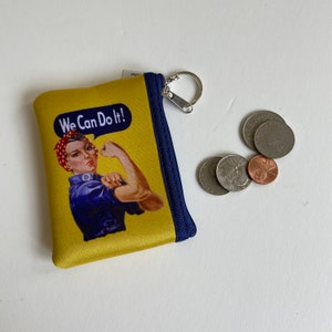 May include: A yellow zippered pouch with a blue trim. The pouch features a vintage image of a woman with the text "We Can Do It!" printed on it. The pouch has a silver zipper pull with a key ring.