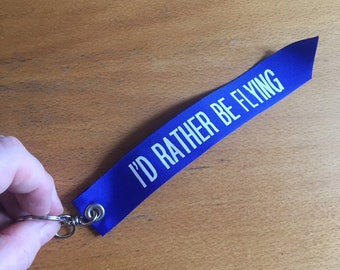 I’d Rather Be Flying Palm-sized Keyfob. Blue ribbon with white lettering. airplane/aviation/pilot gift