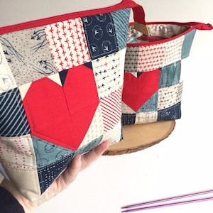 Puede incluir: Dos bolsas de cremallera de patchwork rojo y azul con un diseño de corazón rojo. La bolsa más grande se sostiene en una mano.