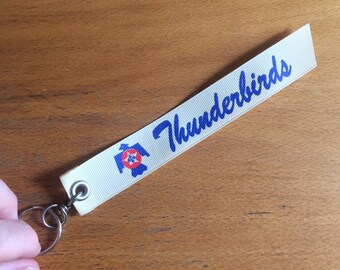Thunderbirds Palm-sized Keyfob. Cream ribbon with blue lettering. airplane/aviation/pilot gift