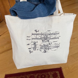 May include: A white canvas tote bag featuring a black and white line drawing of a vintage aircraft design. The design includes the text "Fig 1", "Fig 2", and "Fig 3".