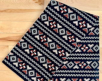 May include: Two pieces of black fabric with a geometric pattern in white, red, and peach. The fabric has a repeating pattern of squares, diamonds, and flowers. The fabric is folded in half and the text "VERITABLE ANGEL REAL" is visible on the bottom edge.