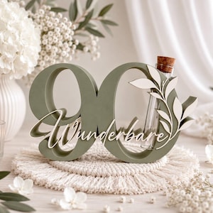May include: A sage green wooden number 90 sign featuring the white cursive text Wunderbare and a decorative white leaf cutout. A clear glass test tube with a cork stopper is integrated into the right side of the number zero.