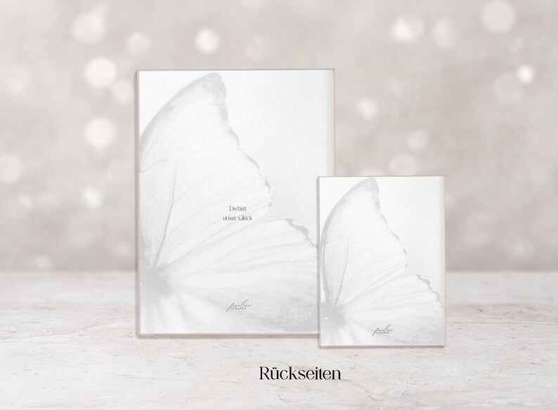 May include: Two white rectangular art prints, one large and one small, feature a butterfly wing design. The prints have the text "Du bist unser Gl&uuml;ck" and "R&uuml;ckseiten".