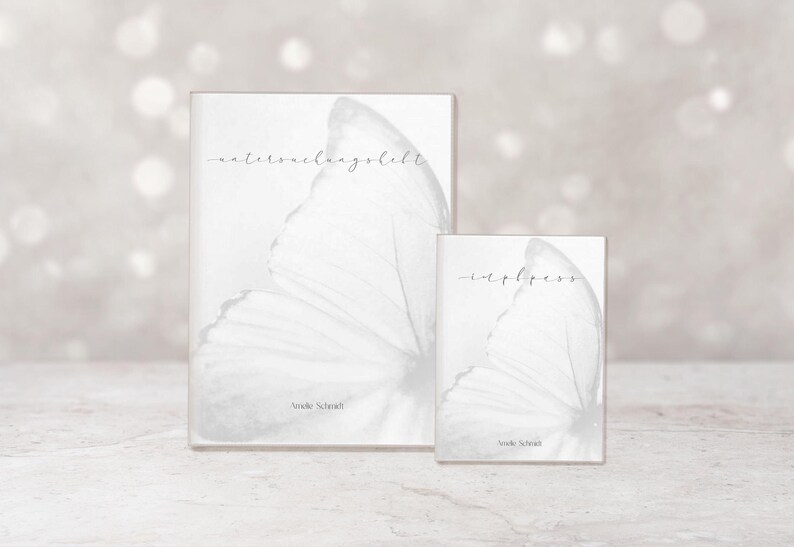 May include: Two white books with butterfly wing designs. The larger book has the text "waterverhaalsel" and the smaller book has the text "hapless". Both books are by Amelie Schmidt.