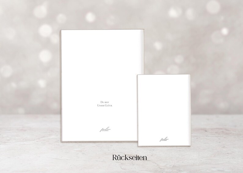 May include: Two white rectangular cards, one larger than the other, are displayed against a soft, blurred background. The larger card has text that reads "Du bist unser Gl&uuml;ck" and the smaller card has the same text. The word "R&uuml;ckseiten" is at the bottom.