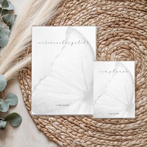 May include: Two white art prints with butterfly wing designs and handwritten text. The larger print reads "maternelangbeft" and the smaller one reads "-eapbess". Both prints are on a woven mat with eucalyptus and pampas grass.