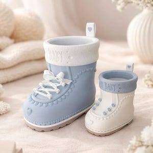 Könnte beinhalten: Zwei dekorative Baby-Stiefel-Pflanzgefäße. Einer ist hellblau mit weißen Schnürsenkeln und Besatz, der andere ist weiß mit blauem Besatz. Beide haben das Wort "Baby" auf dem Bund. Jeder Stiefel hat ein kleines Herzdetail.
