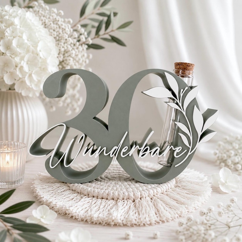 May include: A sage green wooden number 30 sign featuring the white cursive text Wunderbare and a white leaf cutout overlay. A clear glass test tube with a cork stopper is integrated into the right side of the zero, designed to hold small stems.