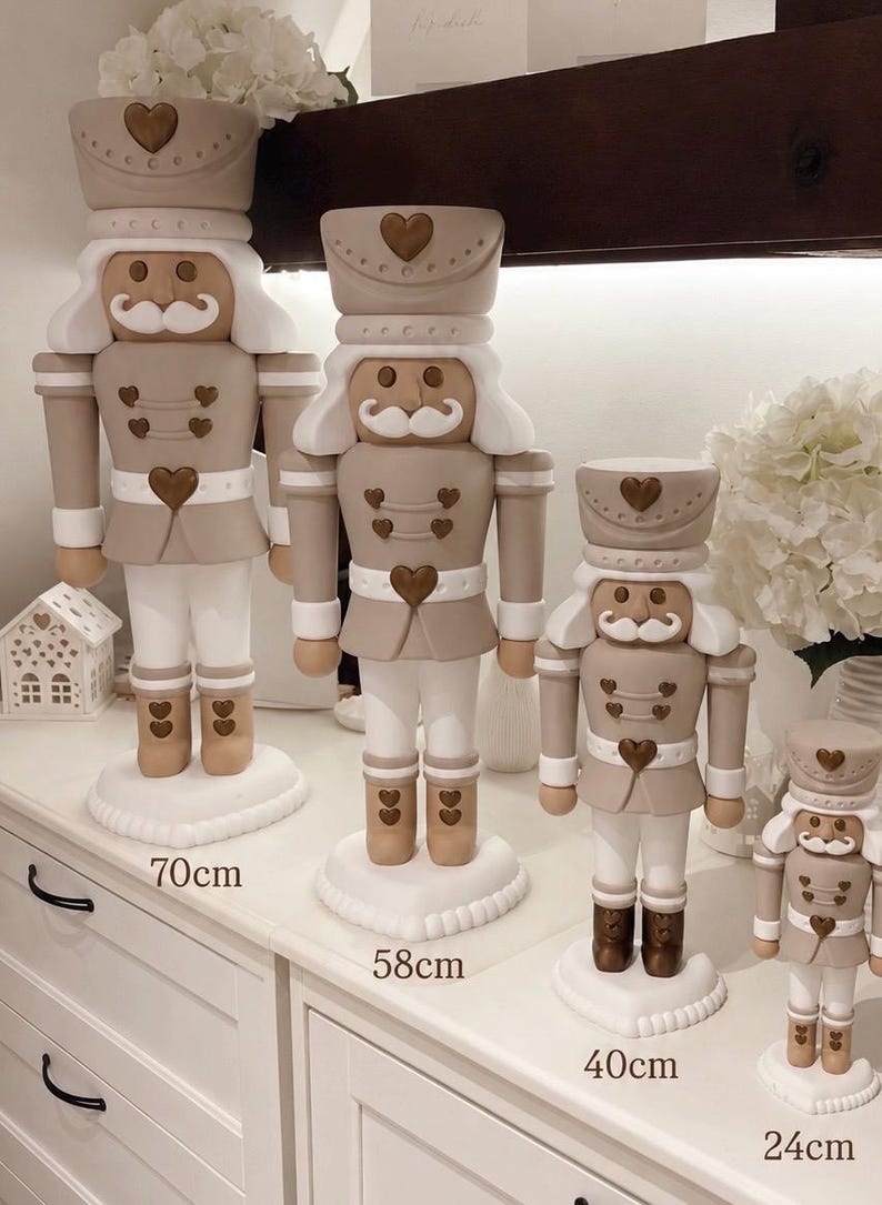 May include: Four nutcracker figures in varying heights of 70cm, 58cm, 40cm, and 24cm. Each figure features a beige and white color scheme with brown heart-shaped accents on the hat, jacket, and boots, and a white mustache and hair.