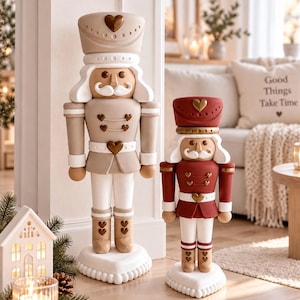 Könnte beinhalten: Zwei Nussknacker-Figuren auf herzförmigen Sockeln. Die größere Figur ist beige und weiß, die kleinere dunkelrot und weiß. Beide haben herzförmige Knöpfe, weiße Schnurrbärte und passende Hüte mit einem herzförmigen Emblem in der Mitte.