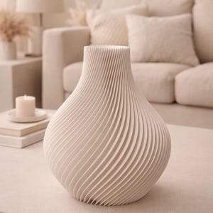 Könnte beinhalten: Eine cremefarbene dekorative Vase mit einem einzigartigen, geriffelten Design. Die Vase hat einen bauchigen Boden und eine ausgestellte Oberseite und steht auf einem neutralfarbenen Tisch. Der Hintergrund umfasst ein Sofa und andere Einrichtungsgegenstände.