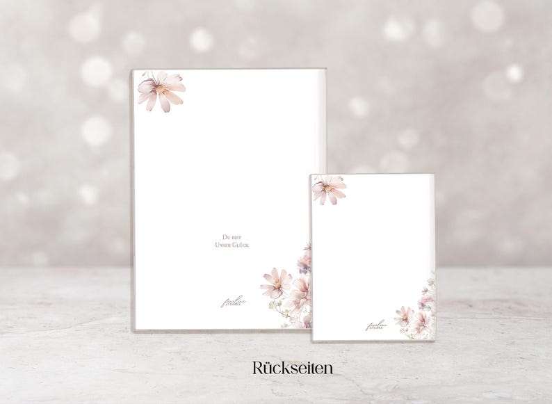May include: Two white notepads with floral accents. The larger notepad has a rectangular shape, while the smaller one is square. Both have a watercolor floral design in the corners and the text "Du bist unser Gl&uuml;ck".