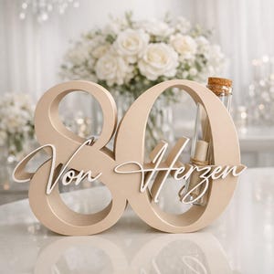 May include: A beige wooden number 80 sign with the white script text Von Herzen attached to the front. A clear glass test tube with a cork stopper and a rolled paper scroll inside is inserted into the upper loop of the number zero.