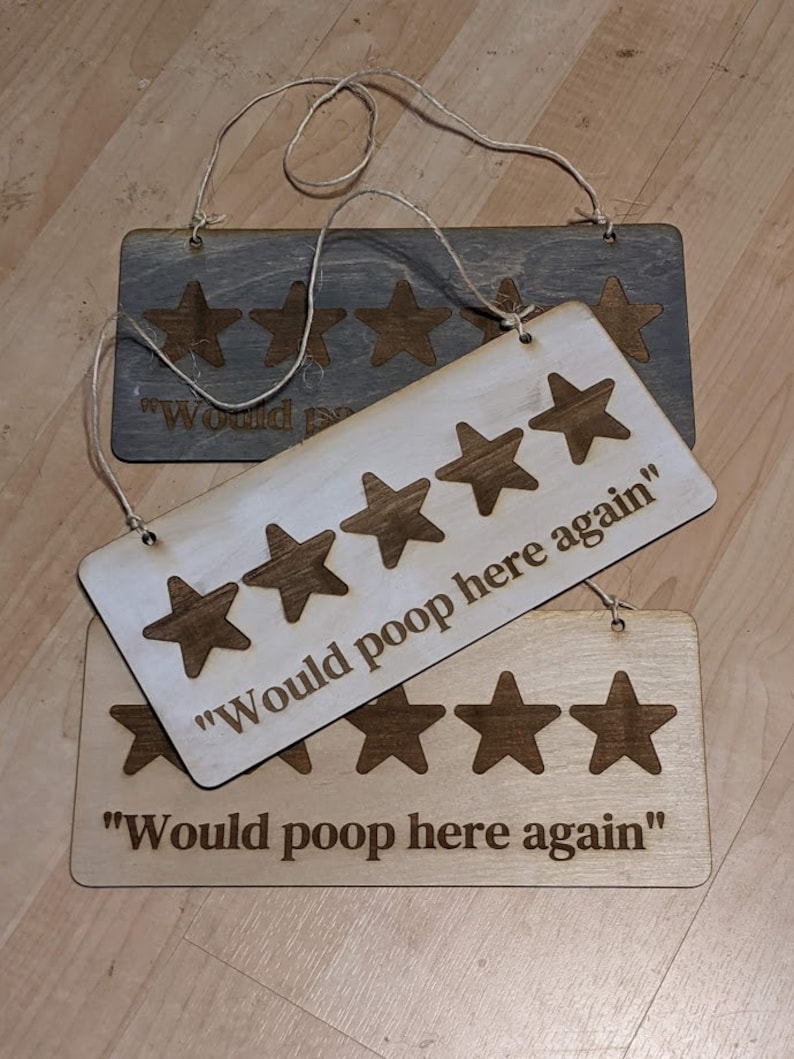 May include: Three wooden signs with the text "Would poop here again" and five-star ratings. The signs are hanging from twine.